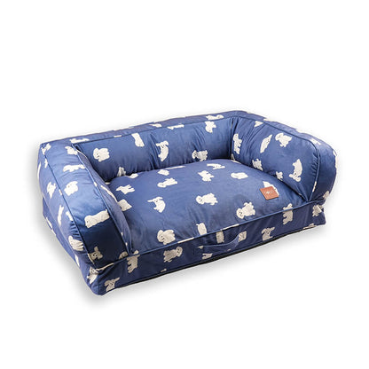 Angled view of the blue Luxe Lounge Sofa Bed for dogs with plush cushioned sides, soft velvety fabric featuring white dog prints, supportive base, and DODO Pet Care logo, isolated on a white background.