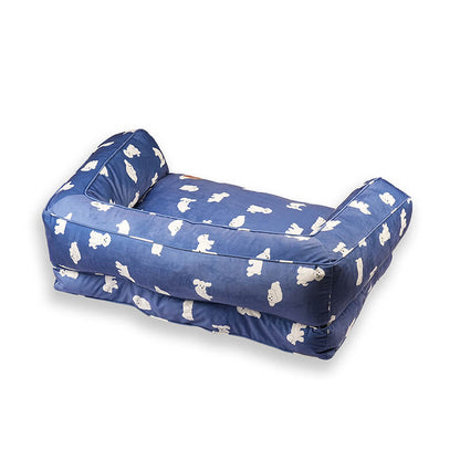 Side view of the blue Luxe Lounge Sofa Bed for dogs featuring raised cushioned bolsters on both ends, soft velvety fabric with white dog prints, thick supportive base, and a cozy rectangular design, isolated on a white background.