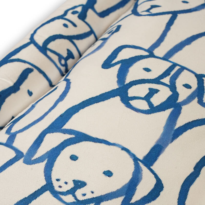 Close-up view of the Paw Pop Bed fabric featuring playful blue hand-drawn dog illustrations on a soft cream cushion, highlighting the smooth plush texture and cozy padding.
