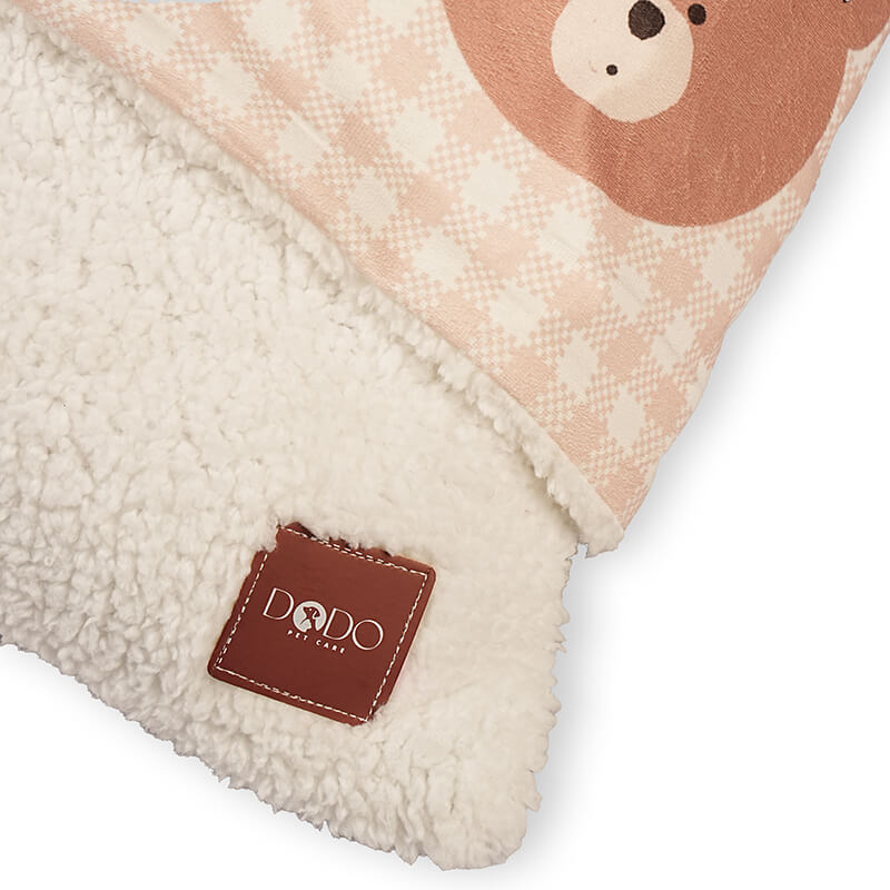 Close-up of the Teddy Snug Bed showing the soft white sherpa inner lining with the DODO Pet Care brand label and teddy print outer fabric, highlighting warmth and comfort for pets.