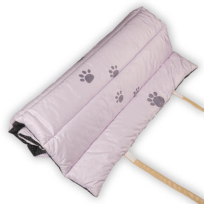 Folded Treatos Travel Mat in soft lavender color with grey paw-print design on the top surface, showing cushioned quilting and beige carry straps, designed for comfortable and portable pet travel use.